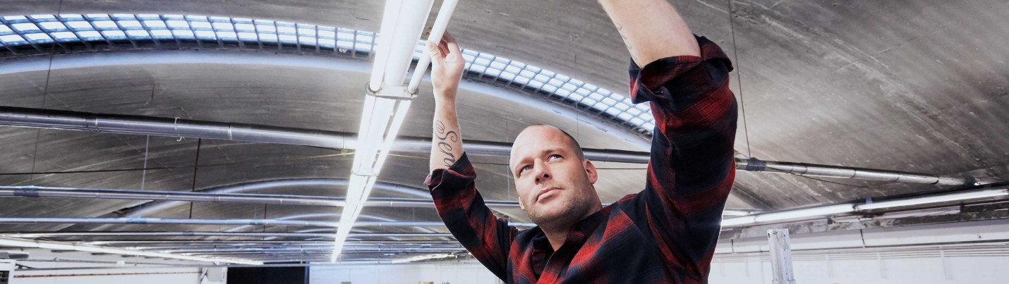 Ein Mann montiert über Kopf eine Philips CorePro LED-Röhre an einer Decke