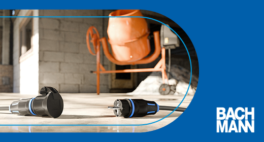 Ein Stecker und eine Kupplung liegen auf dem Boden und im Hintergrund steht ein orangefarbener Betonmischer