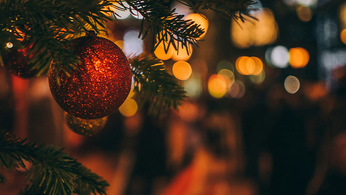 Weihnachtliche Stimmung mit Lichtern im Hintergrund und einer roten Weihnachtskugel im Vordergrund